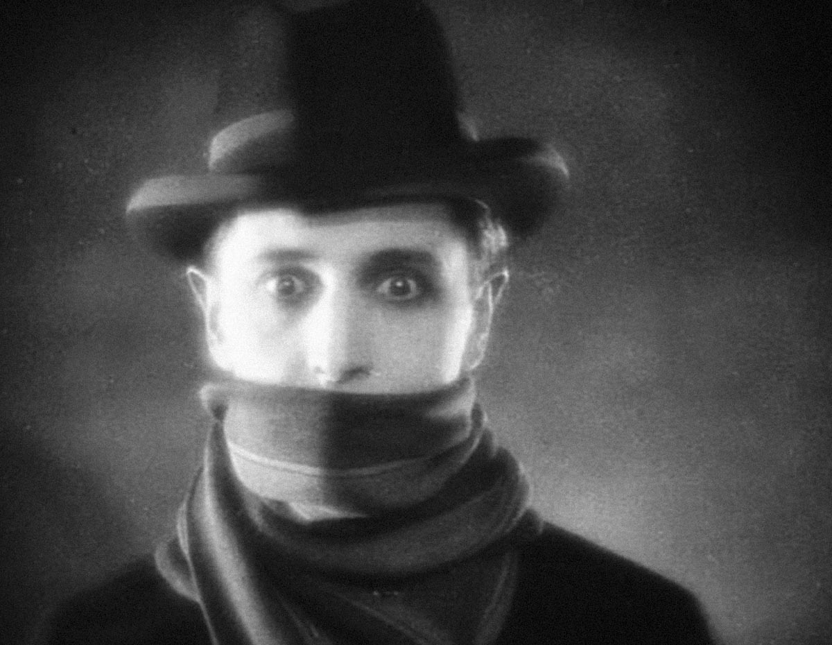 black and white photo of a man wearing a fedora hat and covering his face up to his lips